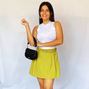 Outfit de mujer con top blanco, falda verde lima y cartera negra.